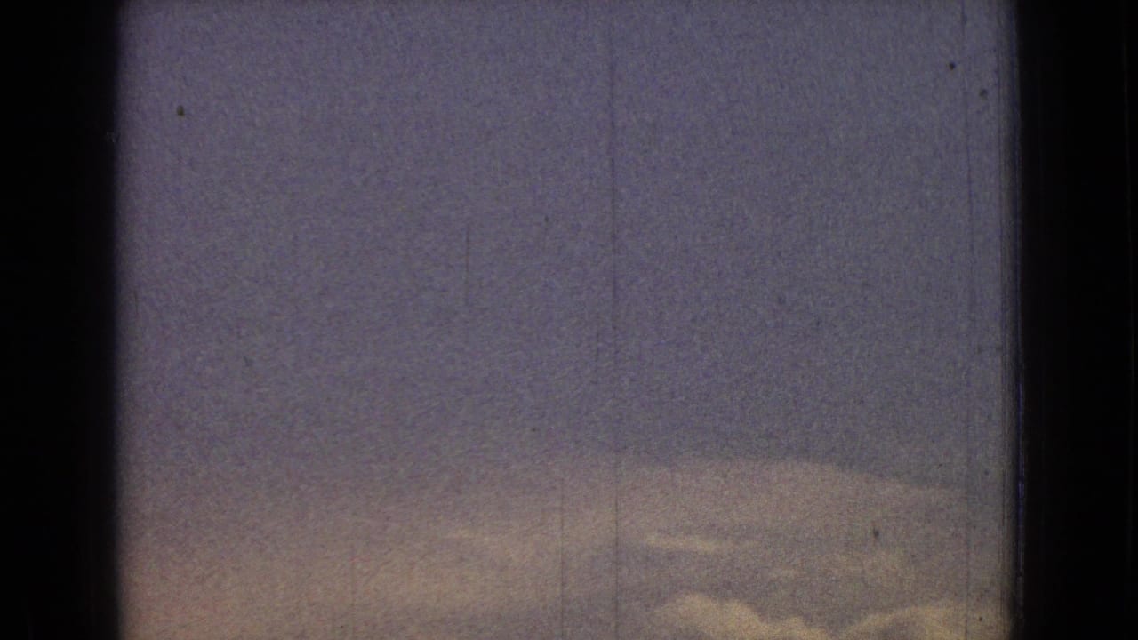 1965 New Jersey home-movie frame showing a pale cloudy sky with a low, faint hill silhouette and dark scan borders.