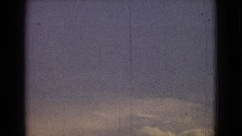 1965 New Jersey home-movie frame showing a pale cloudy sky with a low, faint hill silhouette and dark scan borders.