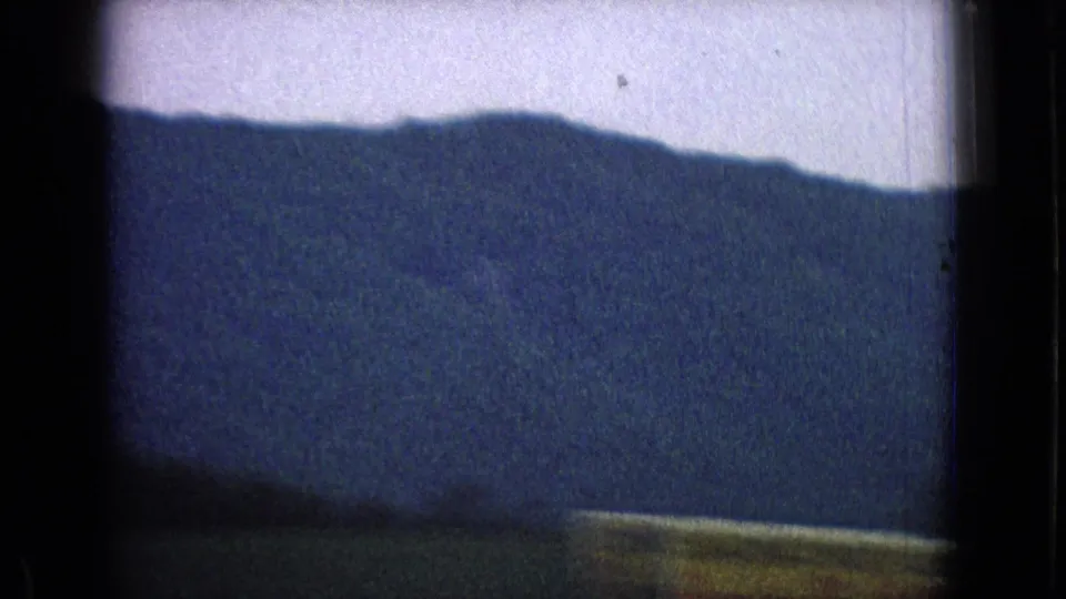 1965 New Jersey 8mm frame showing a blue-toned mountain ridge beyond a darker lower foreground band, with the view softened by motion and film grain.