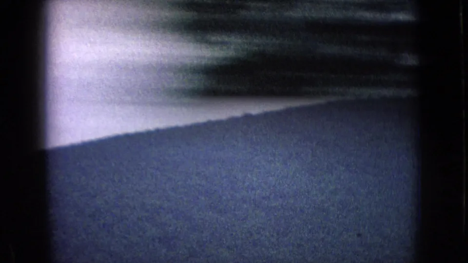 1965 New Jersey home-movie frame showing a mountain slope beneath pale sky, partially crossed by strong motion blur from roadside foreground passing the window.
