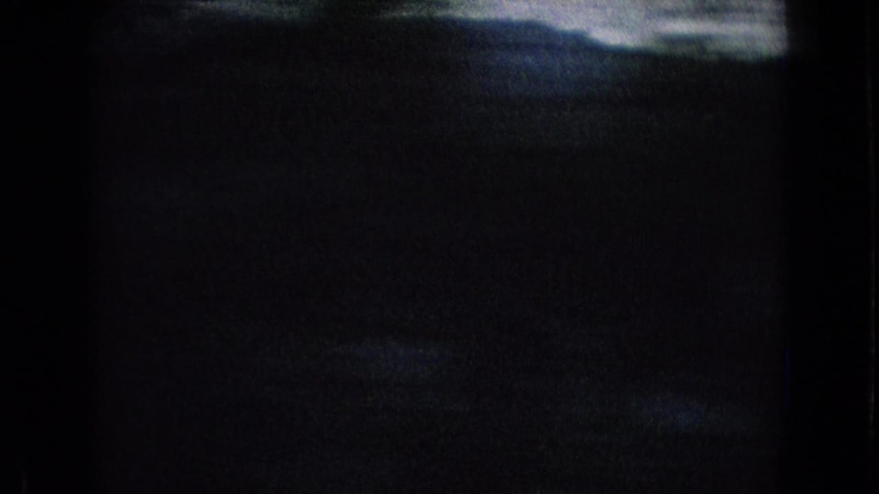 Dark 1965 8mm roadside travel frame showing a barely visible hillside silhouette and pale sky, with heavy black exposure and film-frame edges.