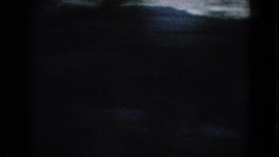 Dark 1965 8mm roadside travel frame showing a barely visible hillside silhouette and pale sky, with heavy black exposure and film-frame edges.