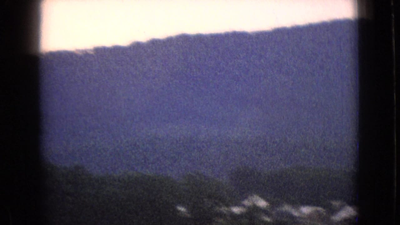 1965 New Jersey 8mm frame showing a blue-green wooded ridge and pale sky, with dark film-frame edges from the home-movie scan.
