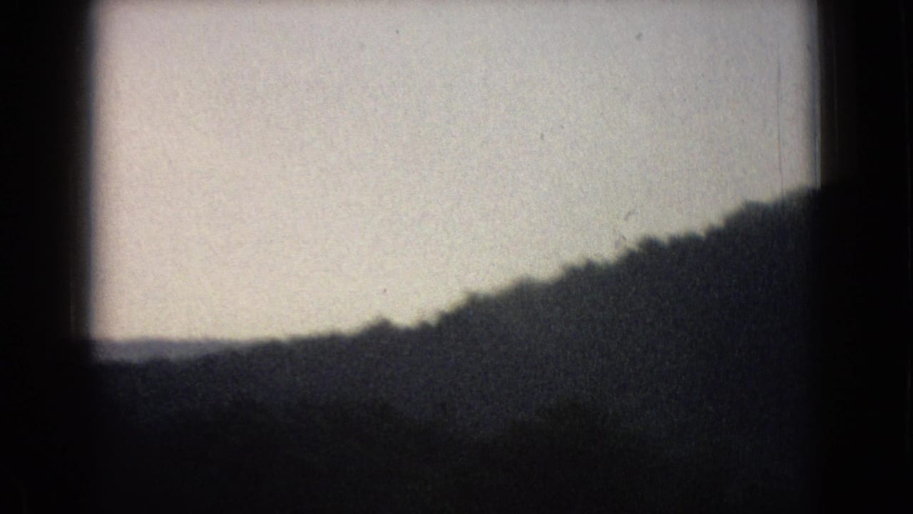 Dark window frame around silhouetted hills beneath a pale sky.