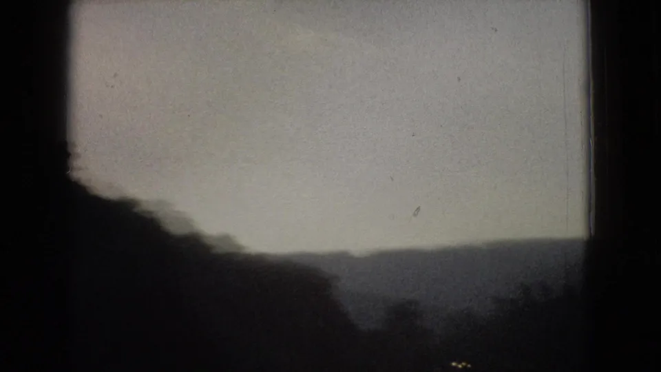 1965 New Jersey 8mm view of rolling wooded hills seen past a dark vehicle-window divider, with soft focus and faded color.
