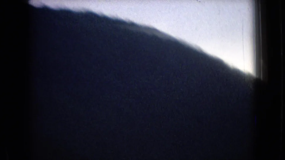 1965 New Jersey home-movie frame with a nearby dark hillside filling the lower view as the vehicle moves past the landscape.