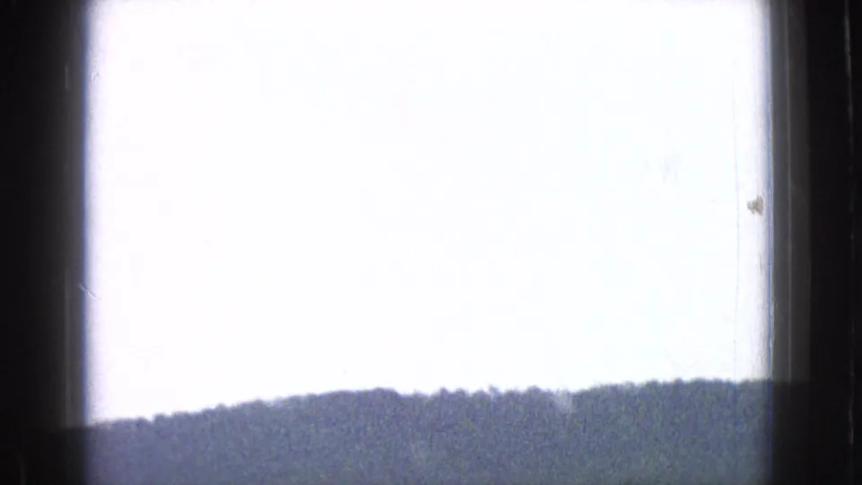 1965 New Jersey 8mm frame showing a low forested ridge below a bright, overexposed sky, bordered by the vehicle interior.