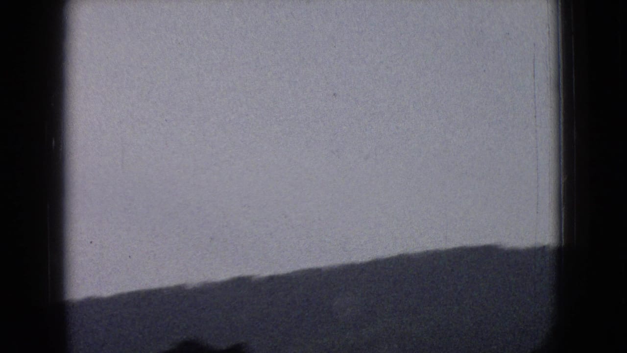 1965 New Jersey home-movie frame showing a silhouetted hillside or mountain ridge under a pale sky from a moving car perspective.