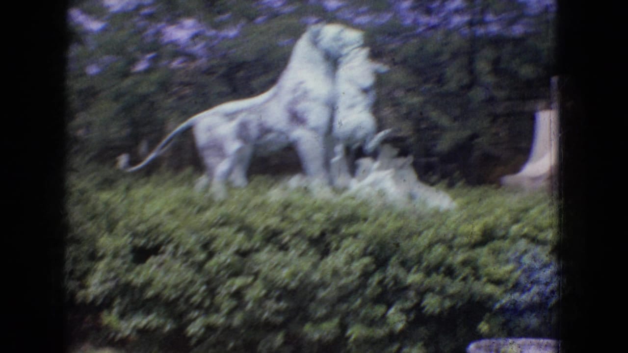Lion statue seen above hedges with trees and masonry in the background.