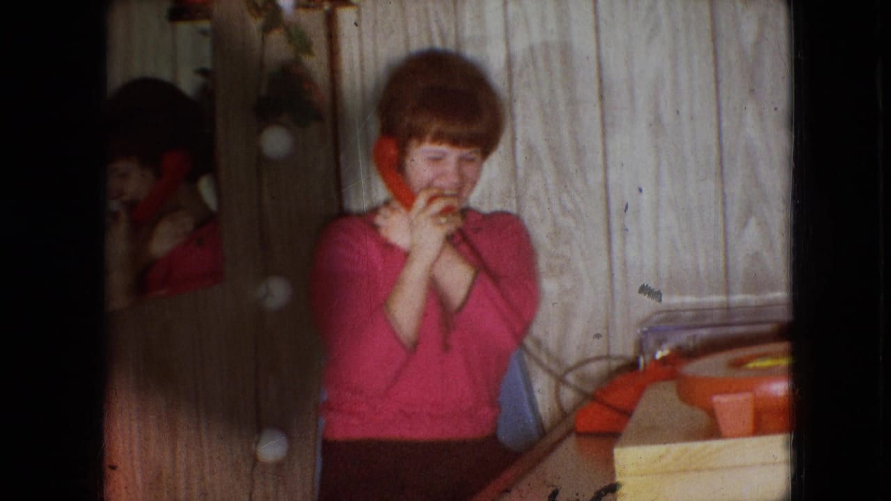 Young woman smiles with a telephone receiver held near her face beside a red rotary phone.