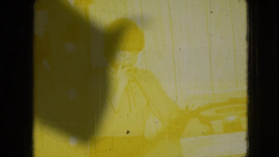 The same room and telephone moment remain faintly visible through a yellow cast, shadowing, scratches, and softened exposure on the 8mm film.