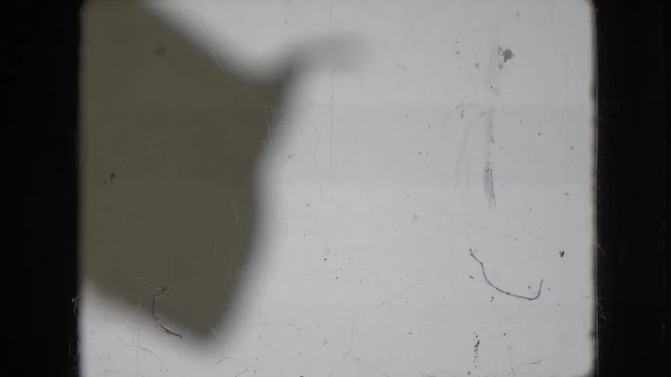 The final frame is largely washed out, showing physical film marks, dust, scratches, and a broad shadow rather than a clear view of the room or person.