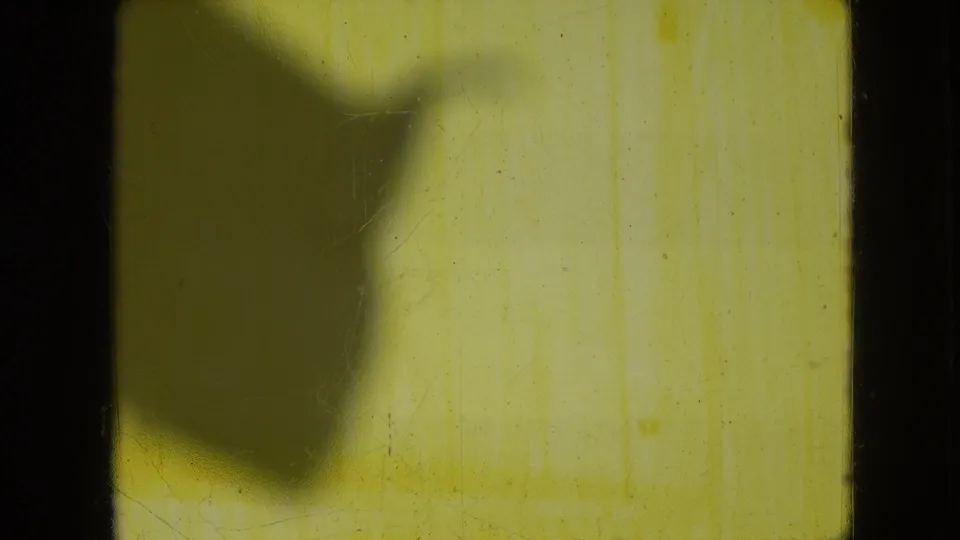 1966 Athens, Ohio 8mm frame showing a soft dark shadow across a yellow-tinted interior wall area with visible film grain and edge marks.