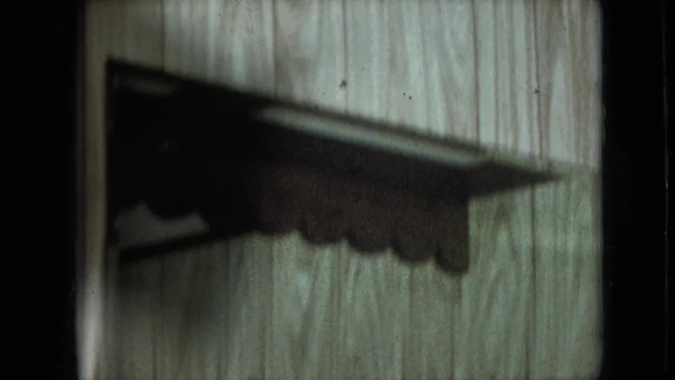 1966 Athens, Ohio 8mm frame showing a dark scalloped shelf-like silhouette cast across vertical wood paneling, with grain and film wear visible.