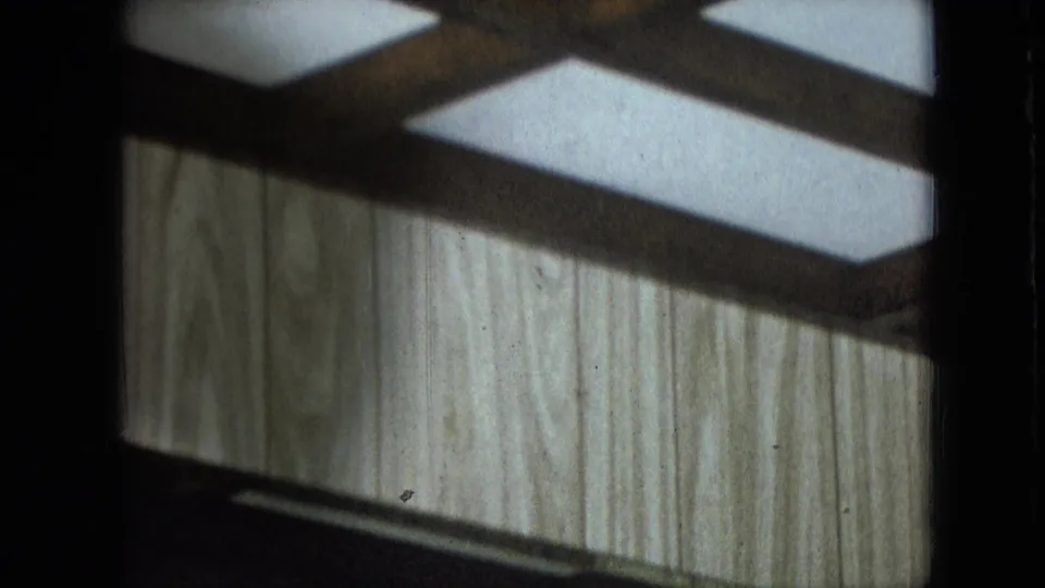 Athens, Ohio 1966 home-movie frame showing light wood paneling, dark framing, and reflected interior light with no clearly visible person.