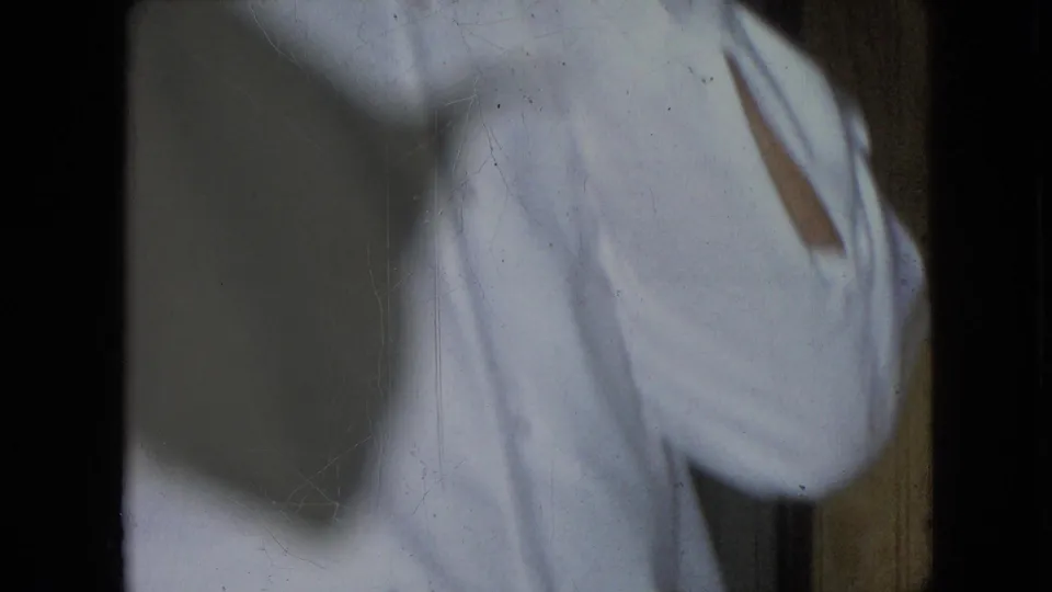 Athens, Ohio 1966 home-movie frame showing the man’s white shirt partly obscured by blur and shadow near a wood-paneled interior.