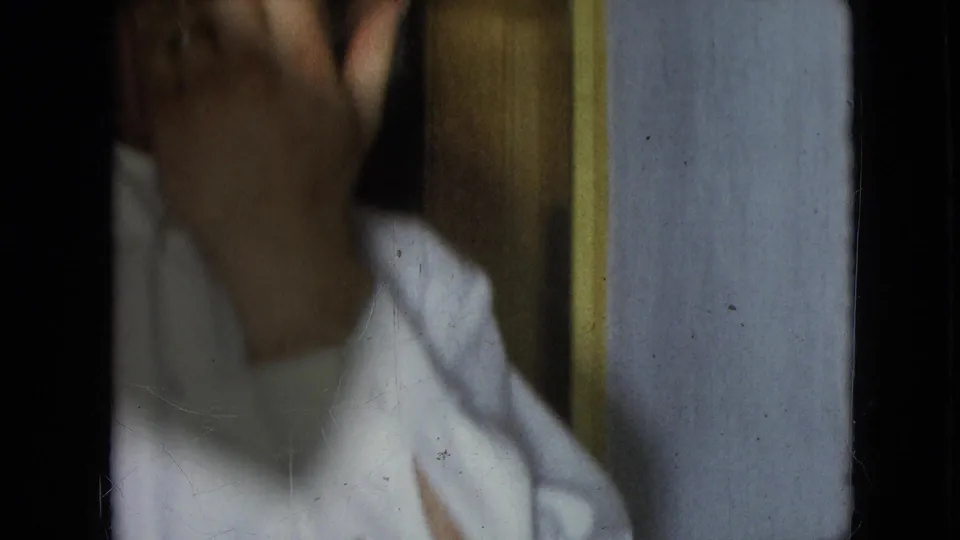 Athens, Ohio 1966 home-movie frame showing an adult man in a white shirt with his hand raised near his face inside a wood-paneled private interior.