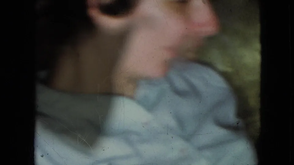 Blurred side view of the young boy in a light blue collared shirt, with handheld 8mm softness and dark frame edges.