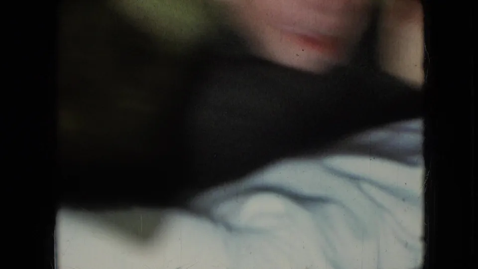 Partly blocked 8mm close-up of the young boy, with a dark foreground shape crossing the frame and pale fabric visible below.