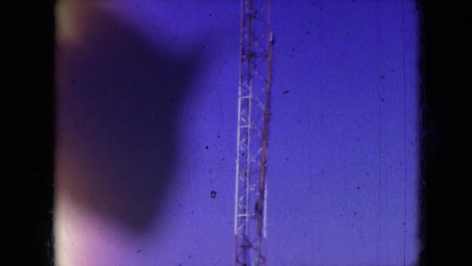 Athens, Ohio 1966 8mm frame with a lattice drilling rig at the right side, blue-tinted sky, and a large dark soft-edged obstruction covering much of the view.