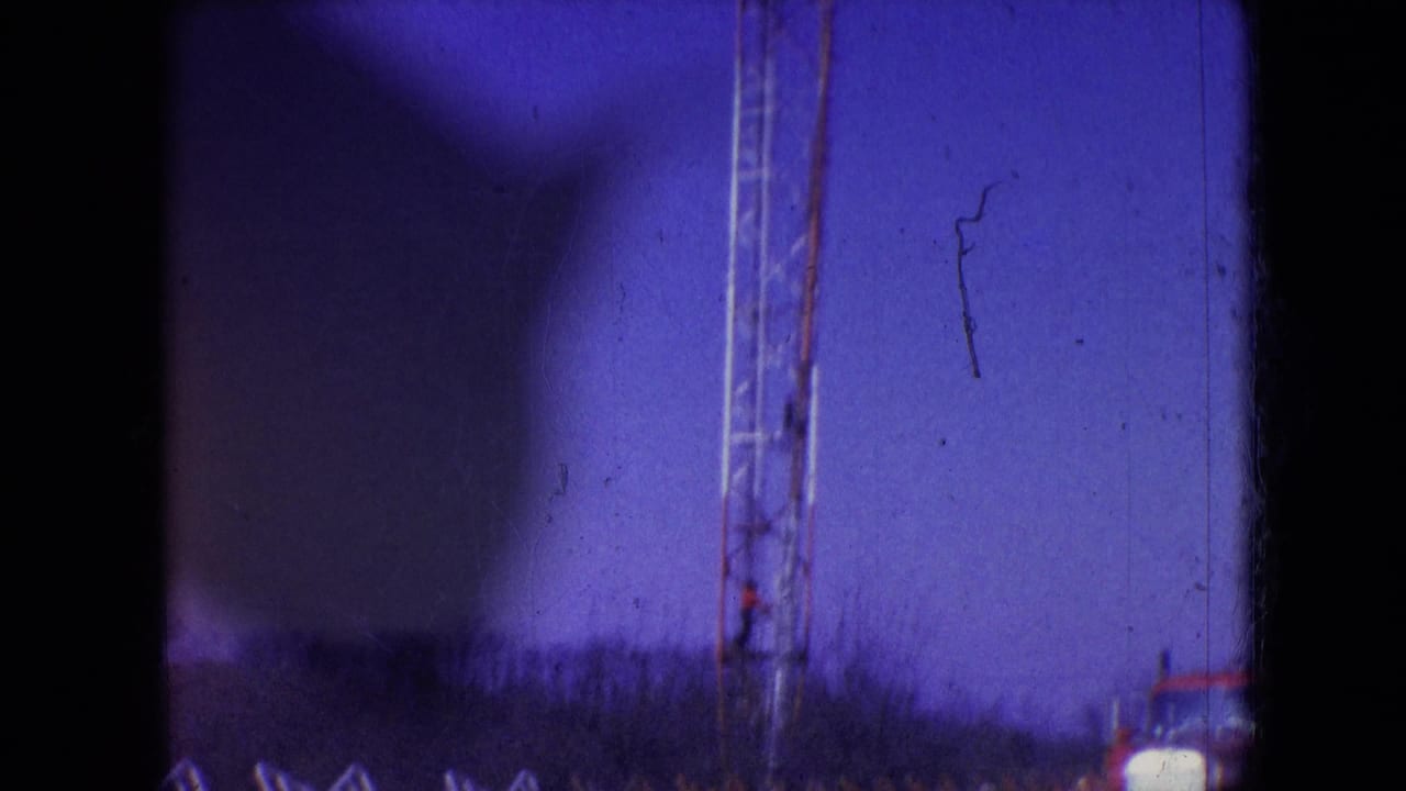 1966 Athens, Ohio home-movie frame showing part of a metal lattice tower and open construction ground with heavy edge shadowing and film wear.