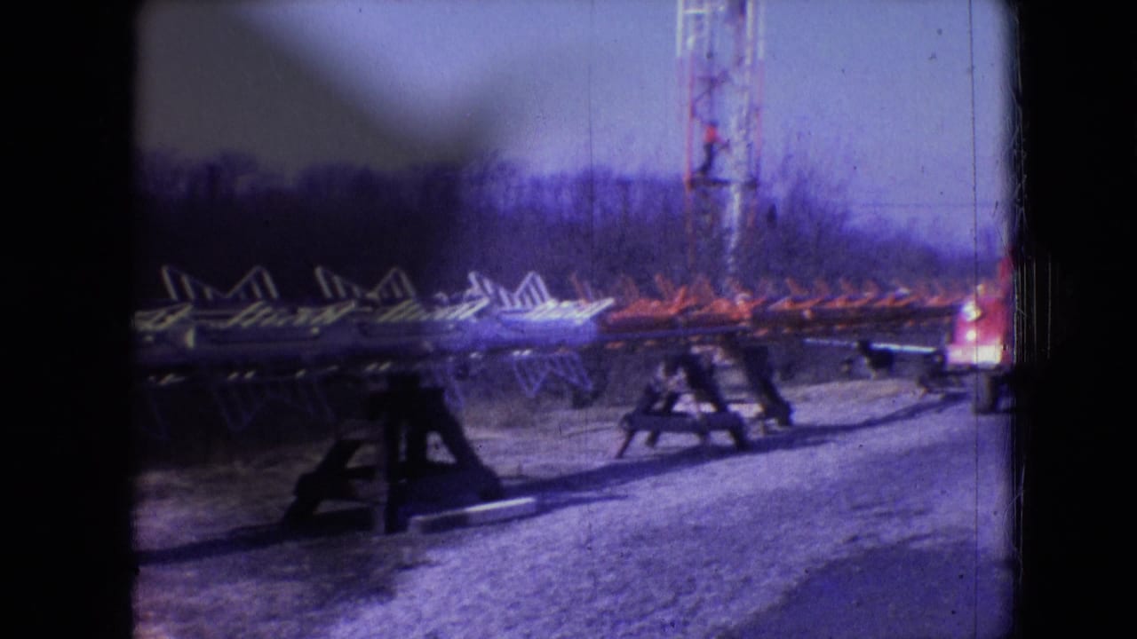 Metal framework sections rest on wooden supports near a tall lattice tower and parked truck.