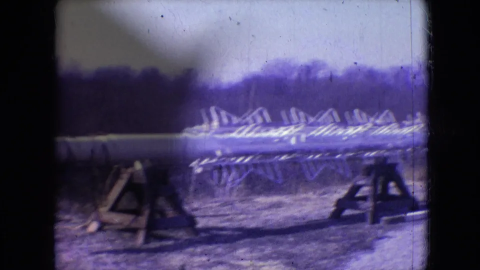 1966 Athens, Ohio frame showing utility tower framework laid across wooden supports in an outdoor construction area, with film grain, scratches, and purple color shift visible.
