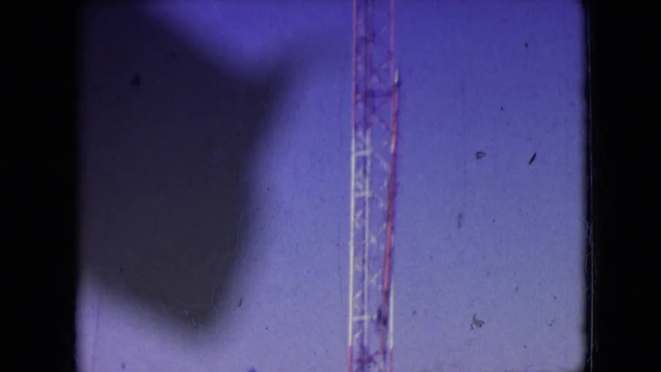 1966 Athens, Ohio 8mm frame emphasizing the vertical lattice communication tower against a blue-purple sky during installation work.