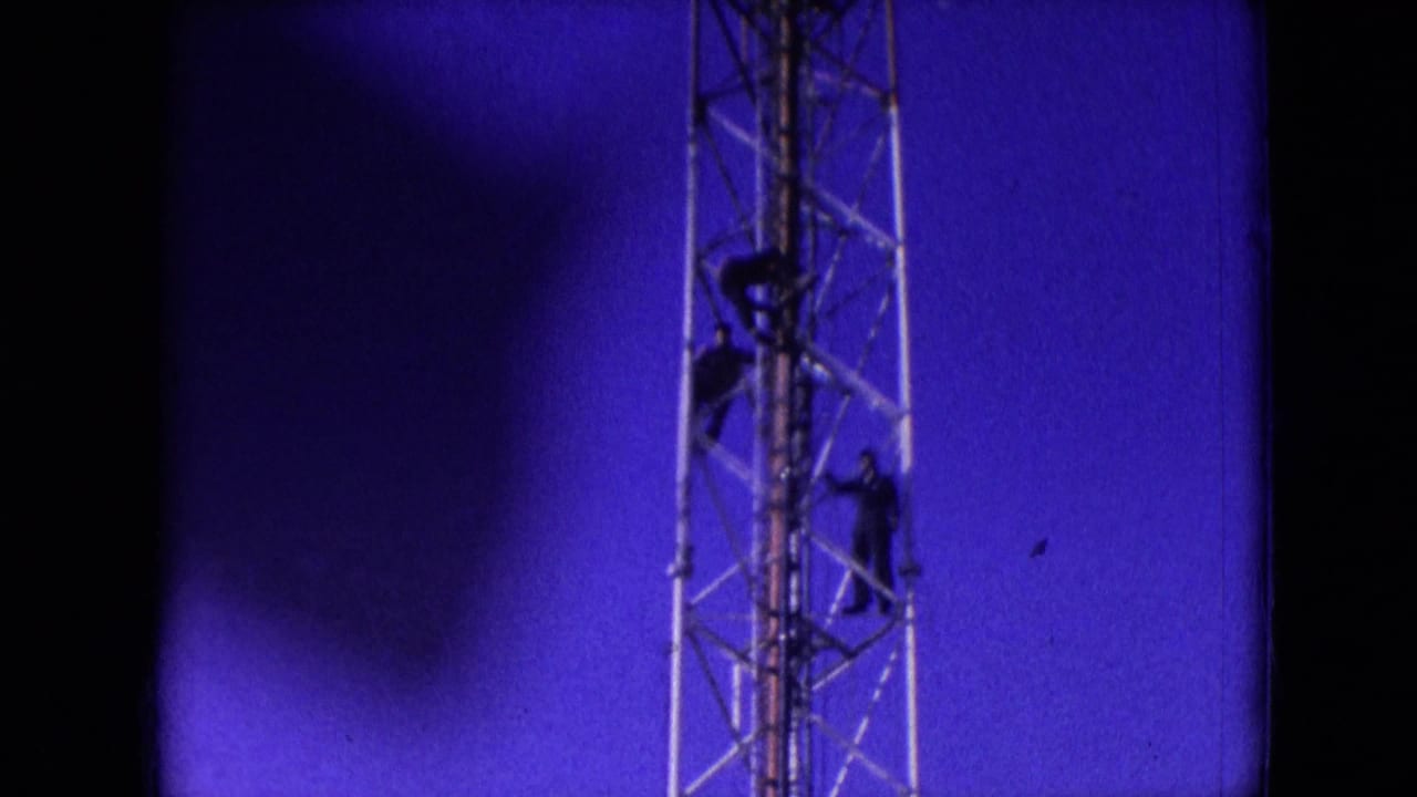 1966 Athens, Ohio 8mm frame showing three dark-clad men on a metal lattice tower, with one higher on the structure and two lower against a saturated blue sky.