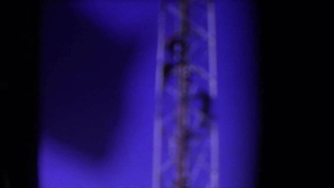 Blurred tower section with a worker high on the metal structure.