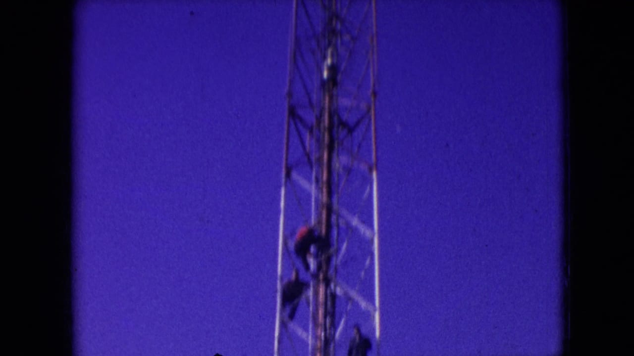Athens, Ohio 1966 home-movie frame showing a worker on a tall lattice radio tower against a saturated blue-purple sky with visible 8mm film borders.