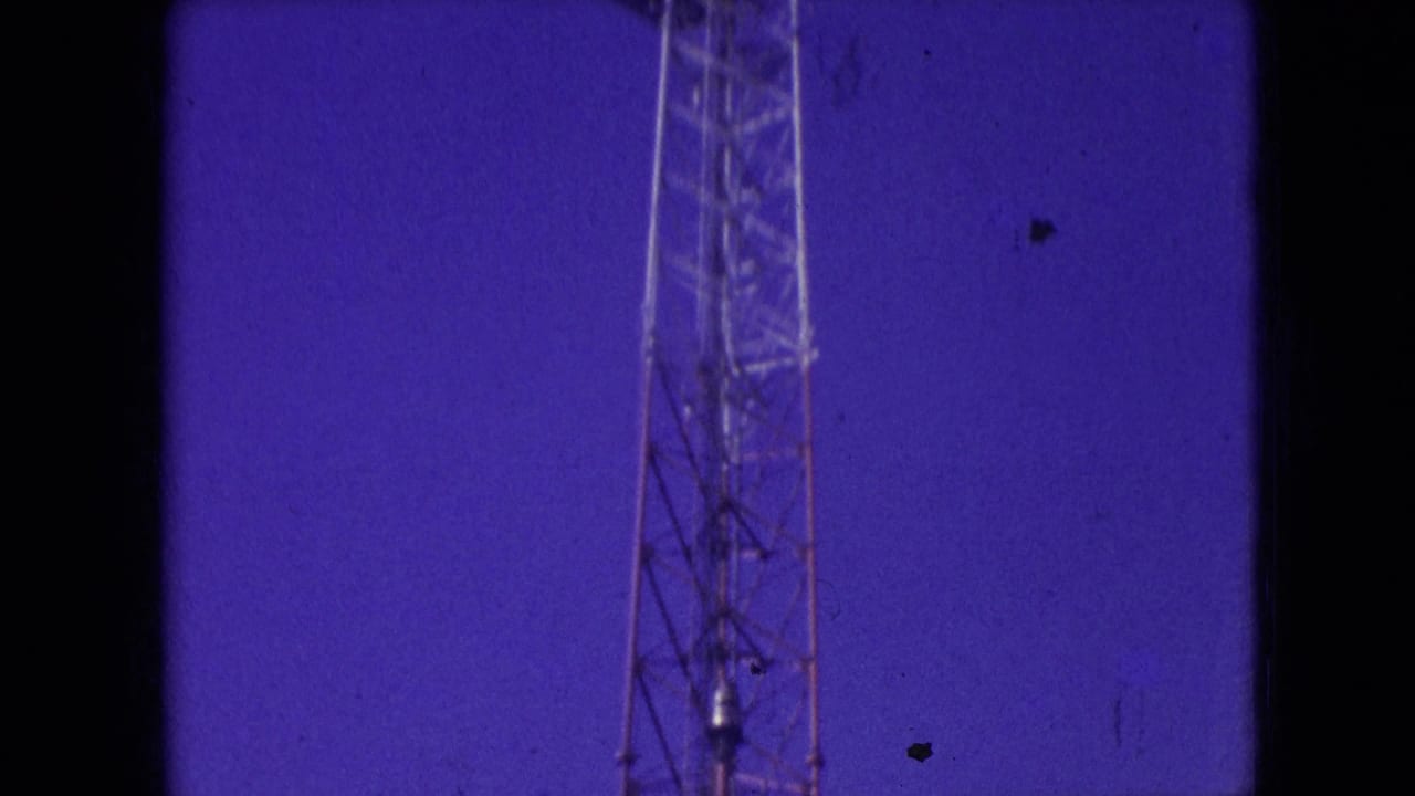 Upper section of a lattice tower rising into a blue-purple sky.