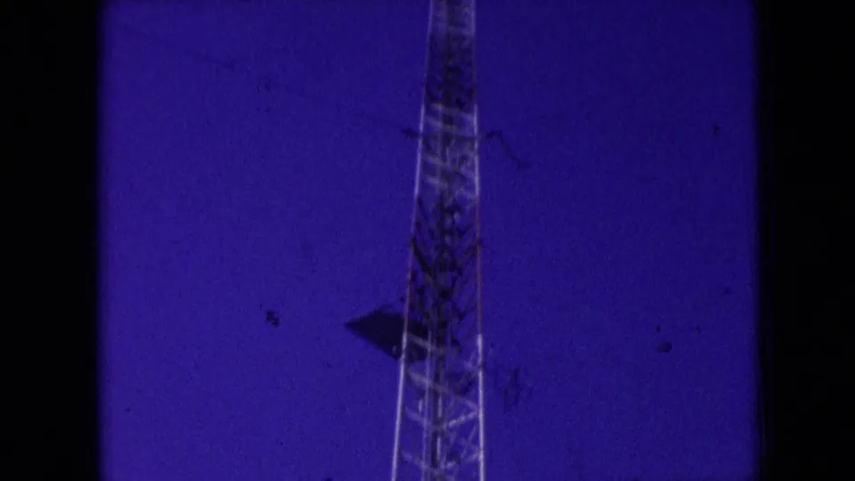 Athens, Ohio 1966 8mm frame showing a radio tower section with a distant worker figure, a dark mounted object, and heavy film texture.