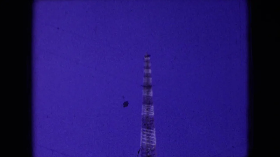A tall lattice-like tower stands against a deep purple sky in 1966 Athens, Ohio home-movie footage, with heavy film tint and dark frame borders.
