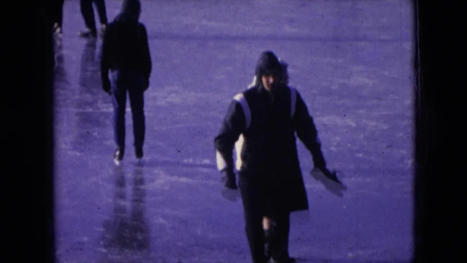 People in dark winter coats and hats skate across an outdoor frozen surface in the Athens, Ohio 1966 home-movie sequence.
