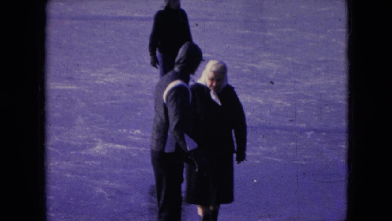 In supplied 1966 Athens, Ohio 8mm footage, a hooded man and a woman in a white headscarf walk together across a frozen snow-covered surface while another figure passes behind them.