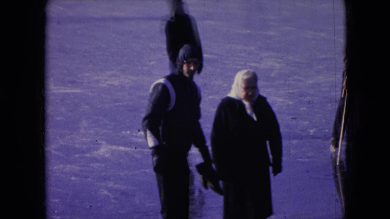 A man and woman in dark winter clothing walk side by side on ice or packed snow.