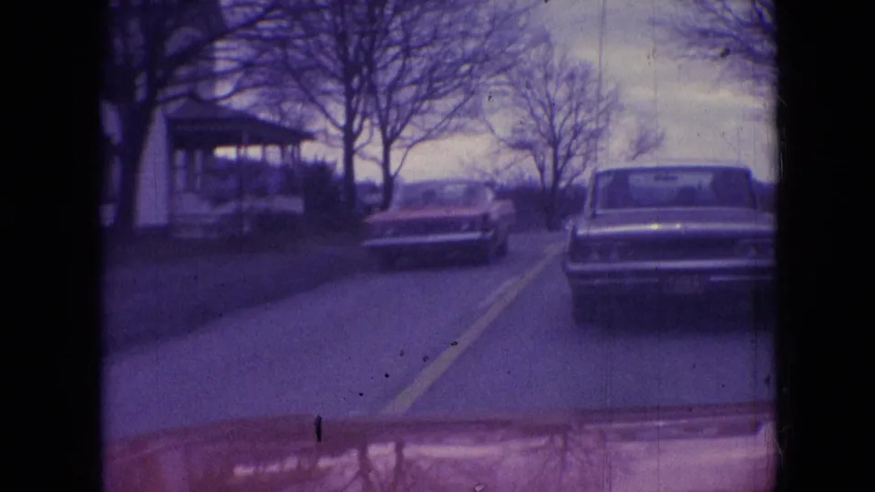 Athens, Ohio 1966 home-movie frame showing an oncoming classic car passing a sedan ahead on a residential two-lane street.