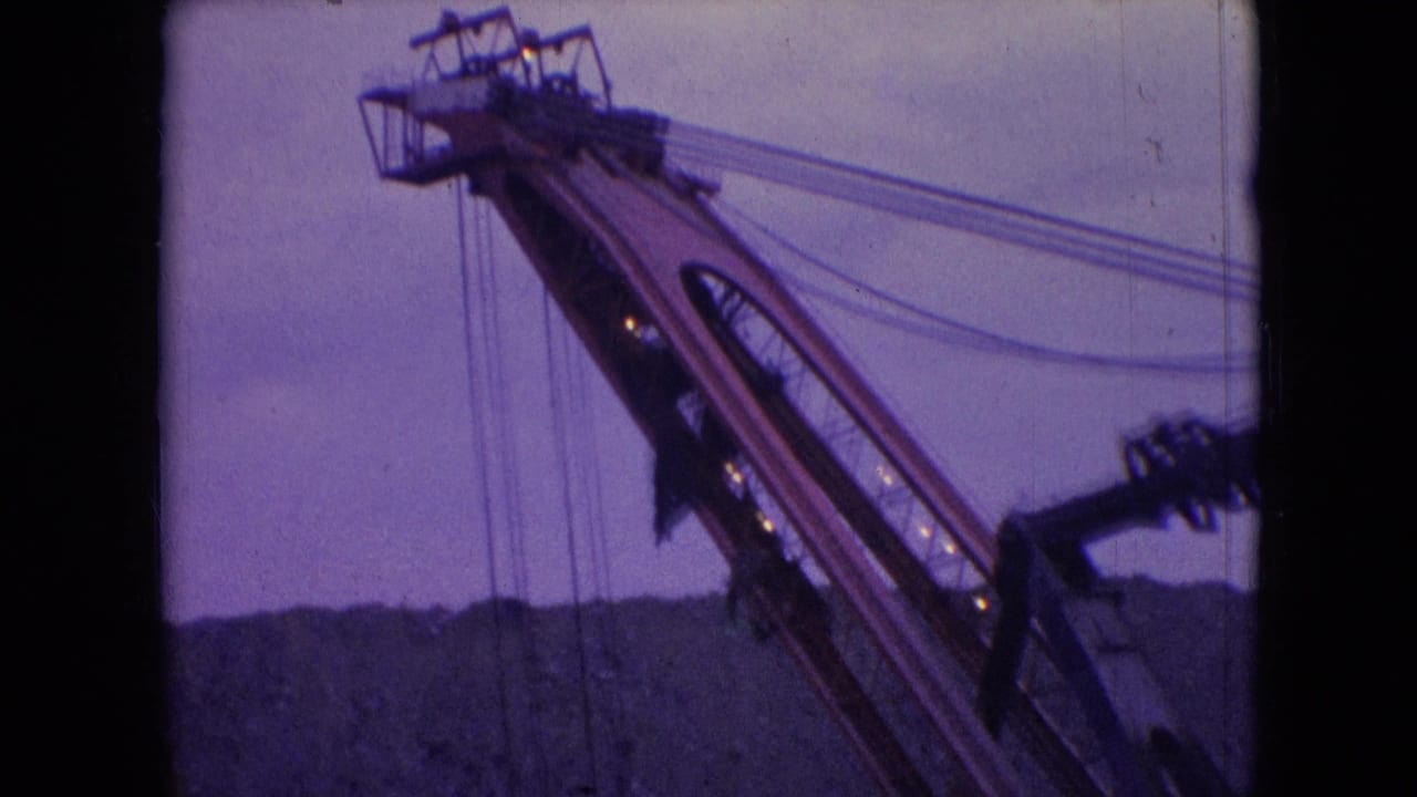 1966 Athens, Ohio 8mm frame showing the upper angled boom of a large construction machine with cables and small lights against a purple twilight sky.