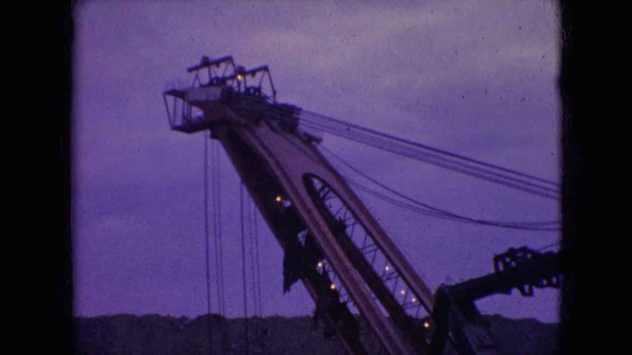 1966 Athens, Ohio 8mm frame of a tall construction crane upper section, with parallel cable lines stretching across a purple-blue evening sky.