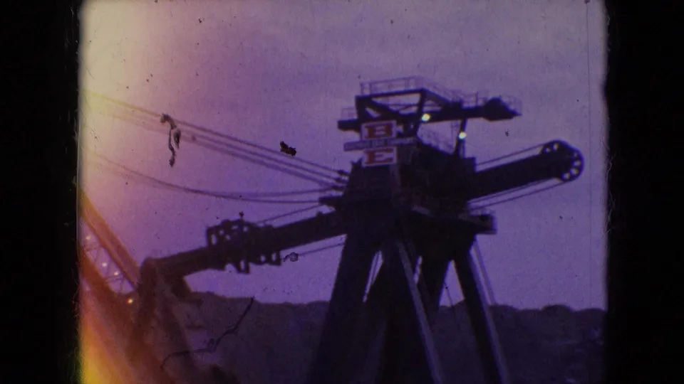 1966 Athens, Ohio 8mm frame of the dark upper head of large construction equipment, with cables, a partial boom, possible markings, and a low ridgeline under twilight sky.