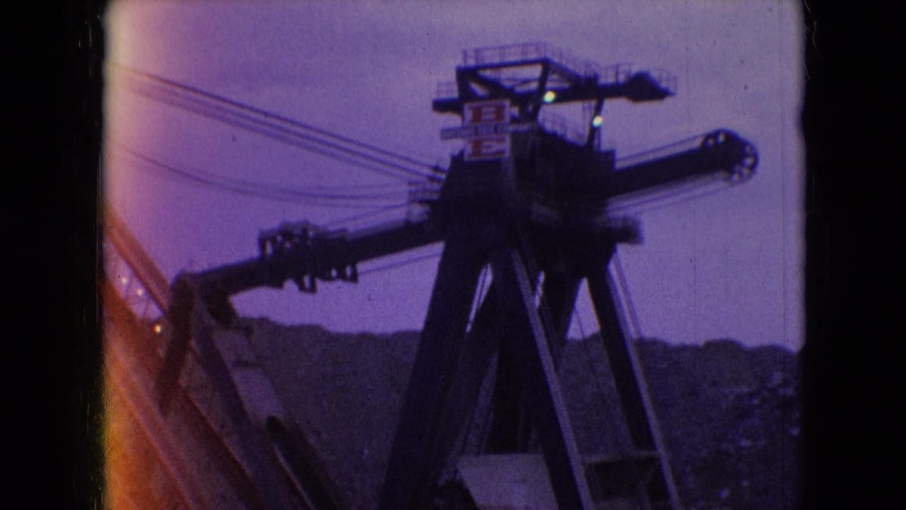 1966 Athens, Ohio 8mm frame showing a large crane-like industrial structure with cables and utility wires silhouetted against a purple twilight sky above a dark ridge.