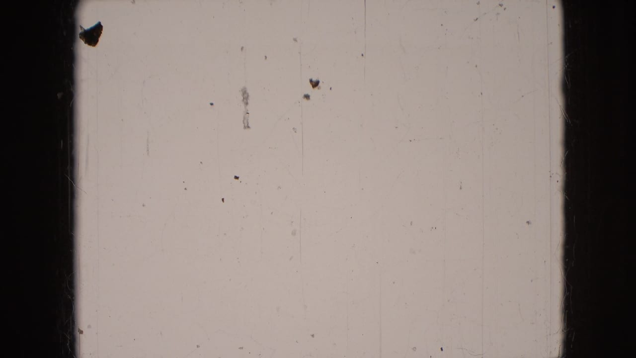 Blank or leader-like 8mm frame with dust, scratches, pale emulsion tone, and dark vertical film borders.