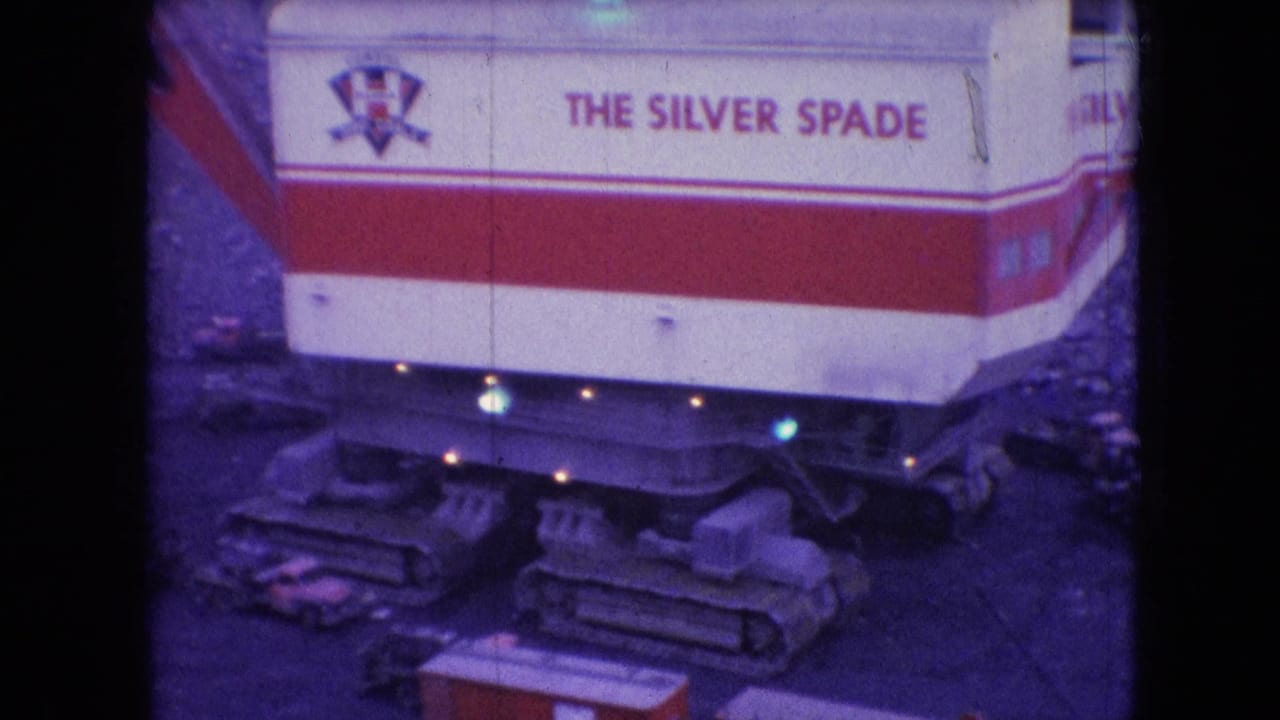 1966 Athens, Ohio 8mm frame showing the red-and-white Silver Spade mining machine from above, with crawler tracks, rocky ground, and small equipment nearby.