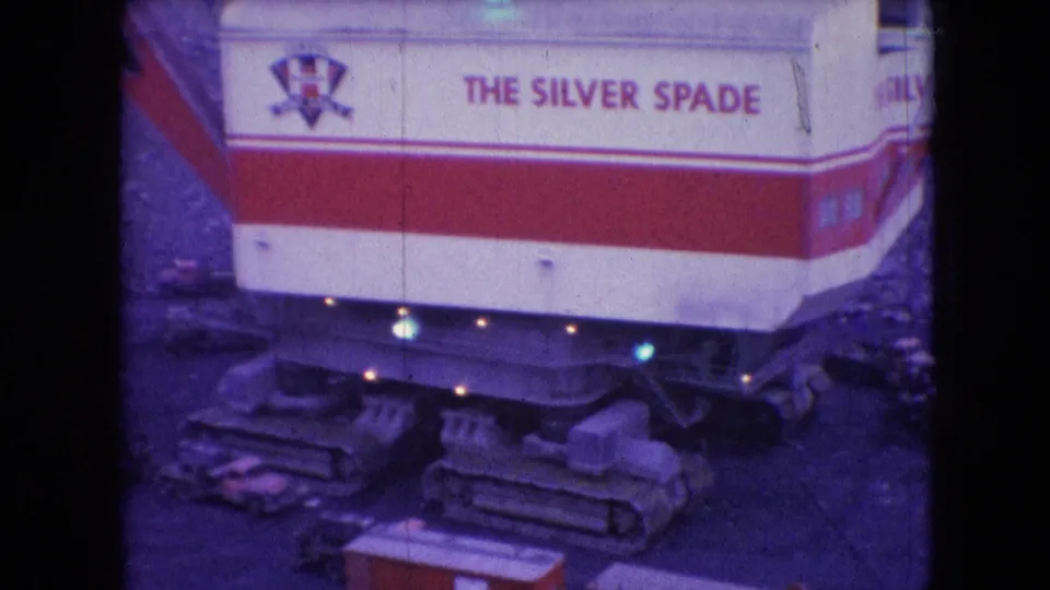 1966 Athens, Ohio 8mm frame showing the red-and-white Silver Spade mining machine from above, with crawler tracks, rocky ground, and small equipment nearby.