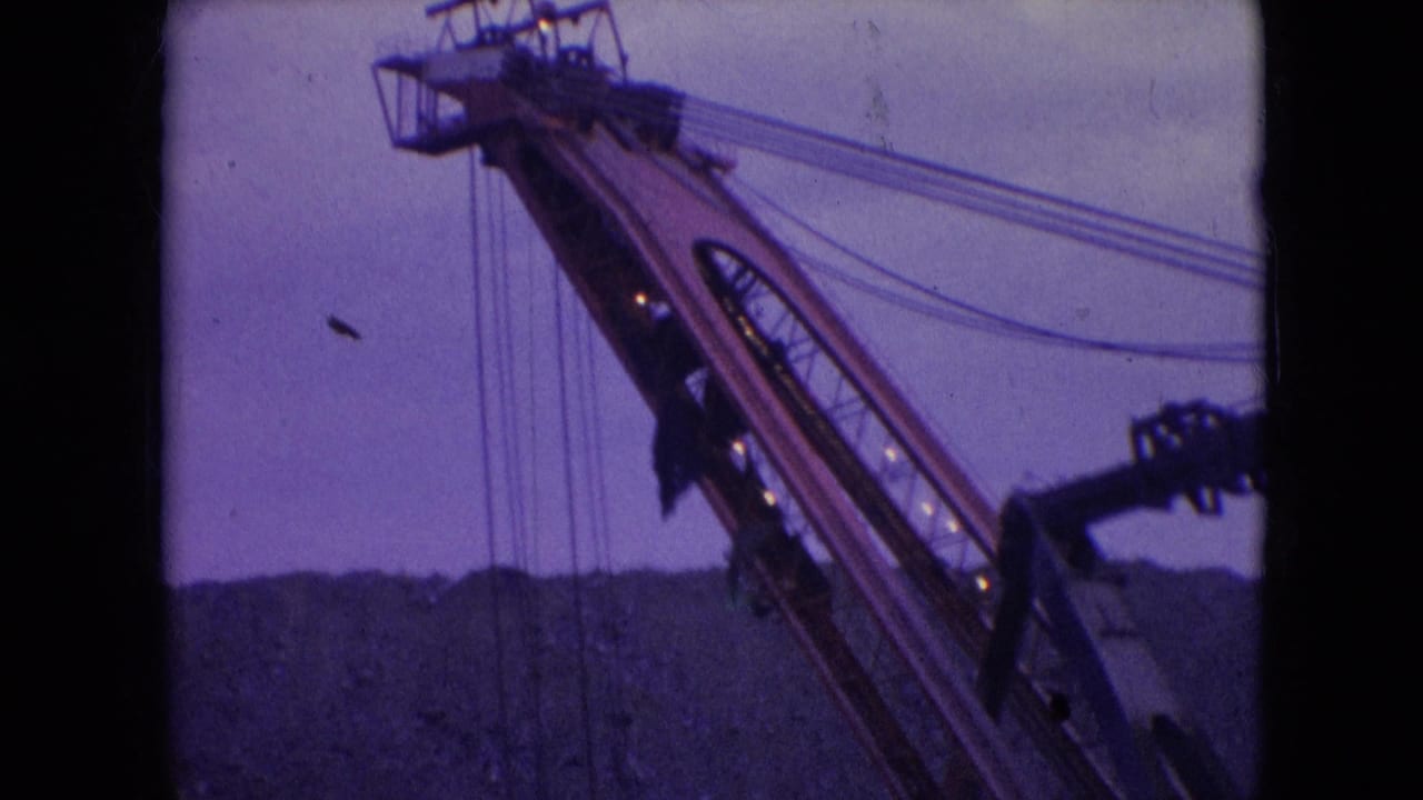 1966 Athens, Ohio frame with the excavator boom lifted above a dark quarry ridge, showing cables, machinery structure, and soft purple film color.