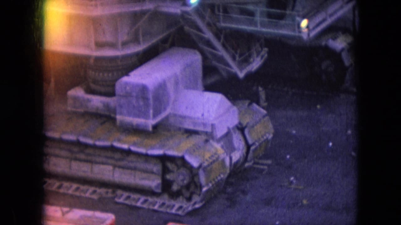 1966 Athens, Ohio home-movie frame showing a large tracked mining machine in a mine yard with purple color shift and yellow light leak at the film edge.