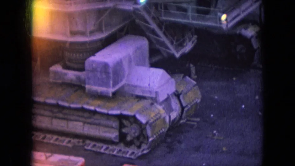 1966 Athens, Ohio home-movie frame showing a large tracked mining machine in a mine yard with purple color shift and yellow light leak at the film edge.