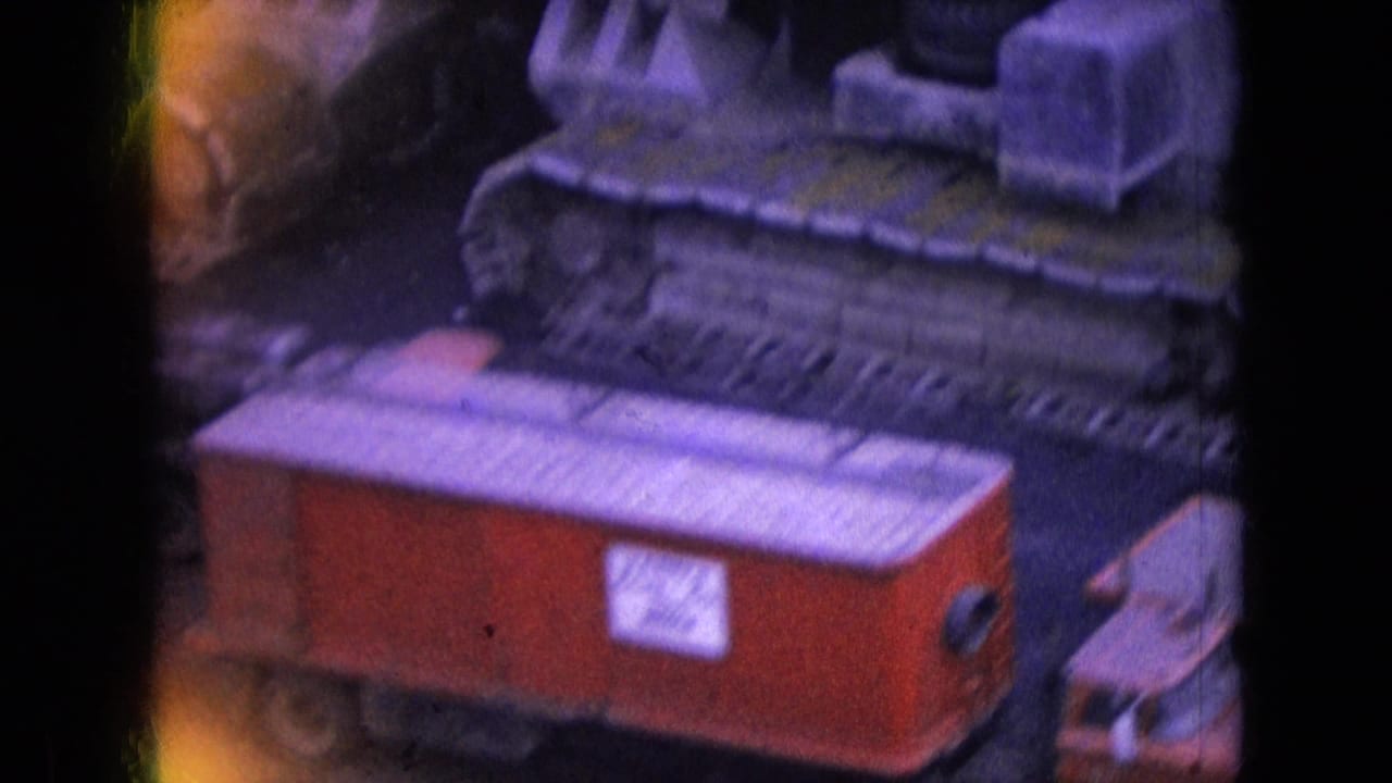 Red coal railcar beside tracked mining equipment.