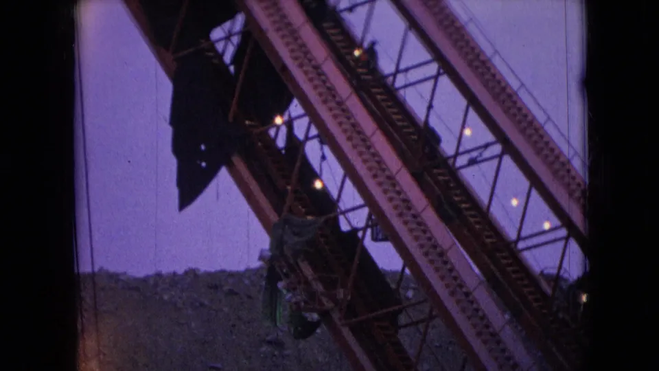 1966 Athens, Ohio 8mm frame showing a diagonal steel crane boom with cables and dark structural details silhouetted against a purple twilight sky.